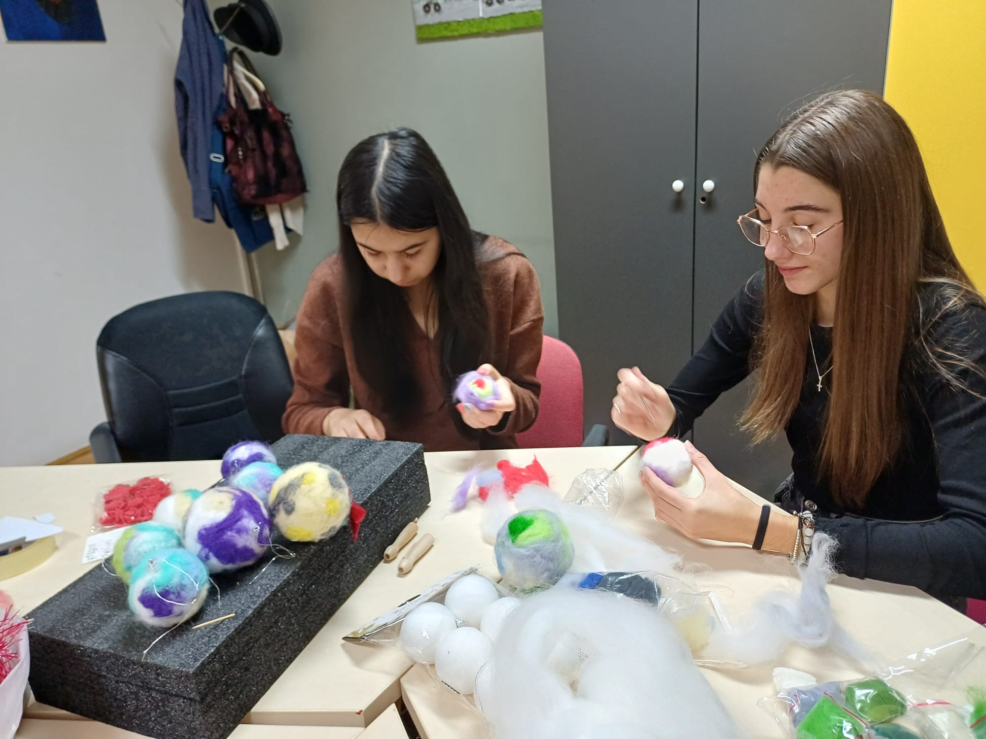Korisnice rukama oblikuju kuglicu od vune za božićni ukras na stolu punom materijala.
