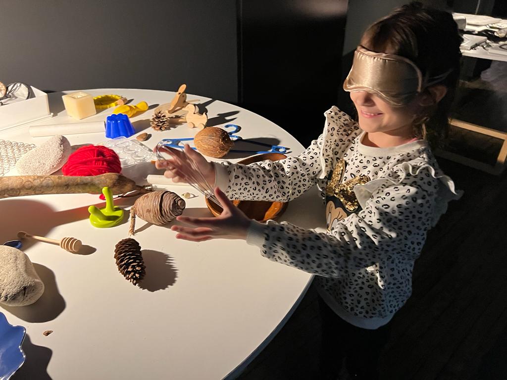 Slika djevojčice kako s povezom na očima istražuje svakodnevne predmete pokušavajući ih prepoznati